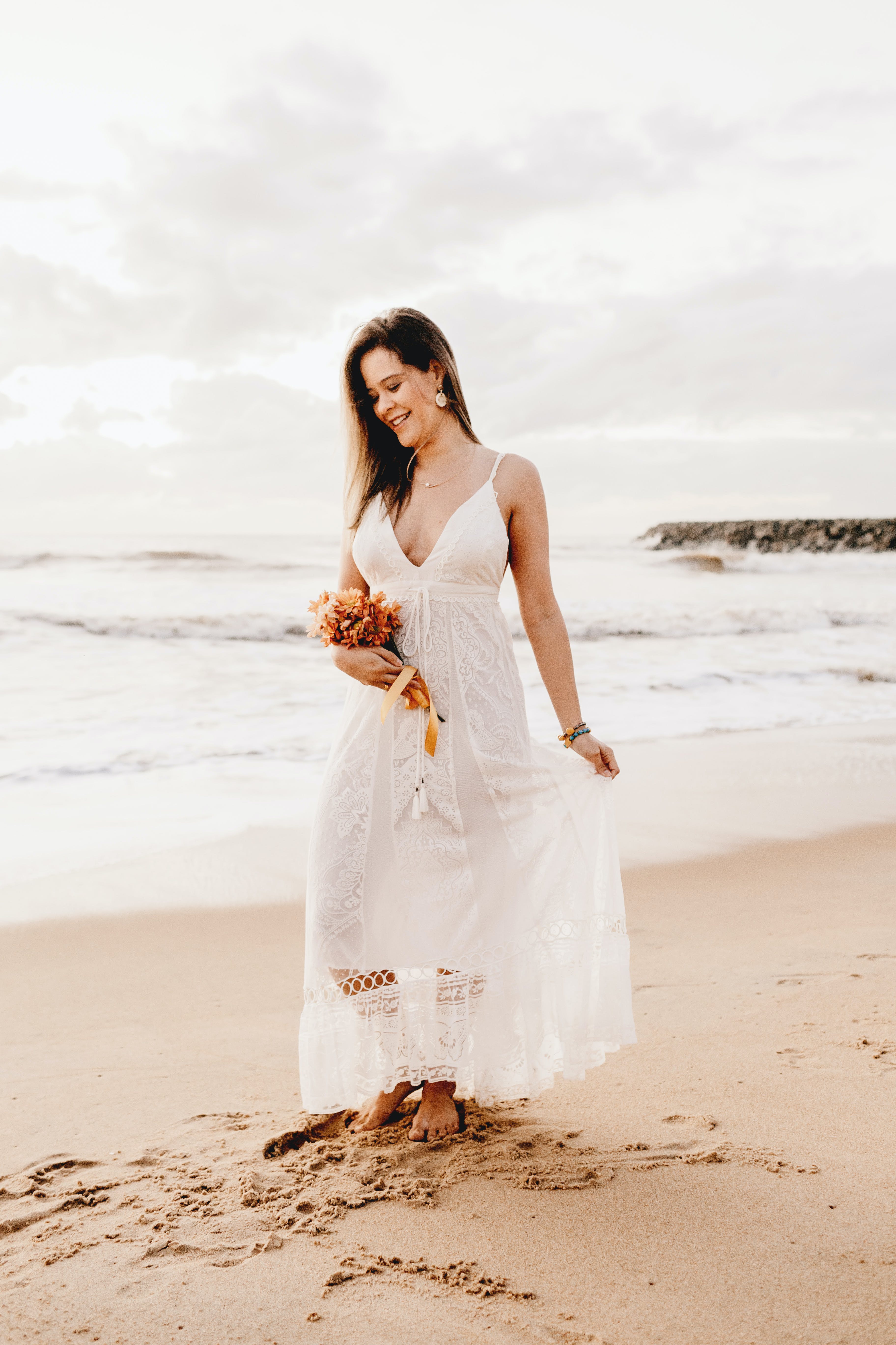 Free Woman Wearing White Spaghetti Strap Dress Holding Flower Bouquet While Standing Near Seashore Stock Photo